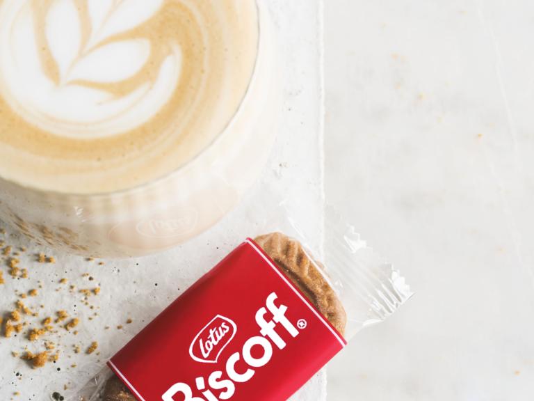Individually wrapped Lotus Biscoff biscuit beside a coffee; serving suggestion